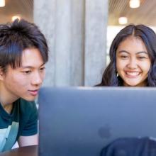 Two students looking at a laptop and smiling