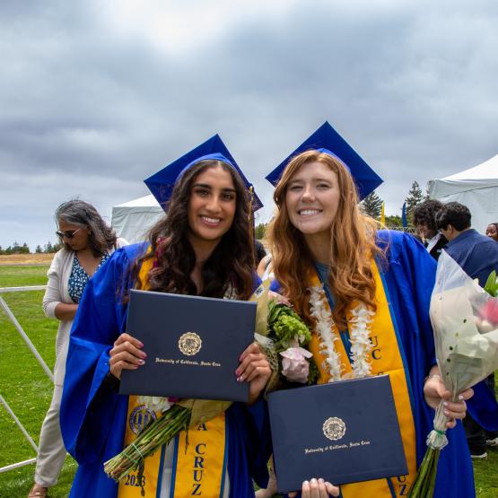 Two students wearing graduation gowns and holding their degrees